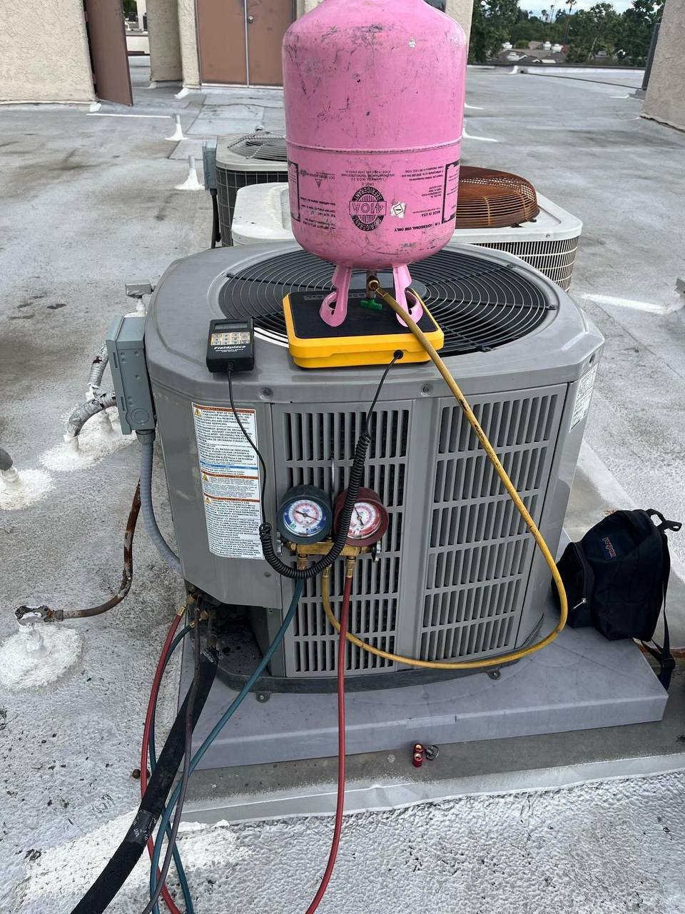 ECO Heating & Cooling technician servicing AC unit with refrigerant gauges on rooftop